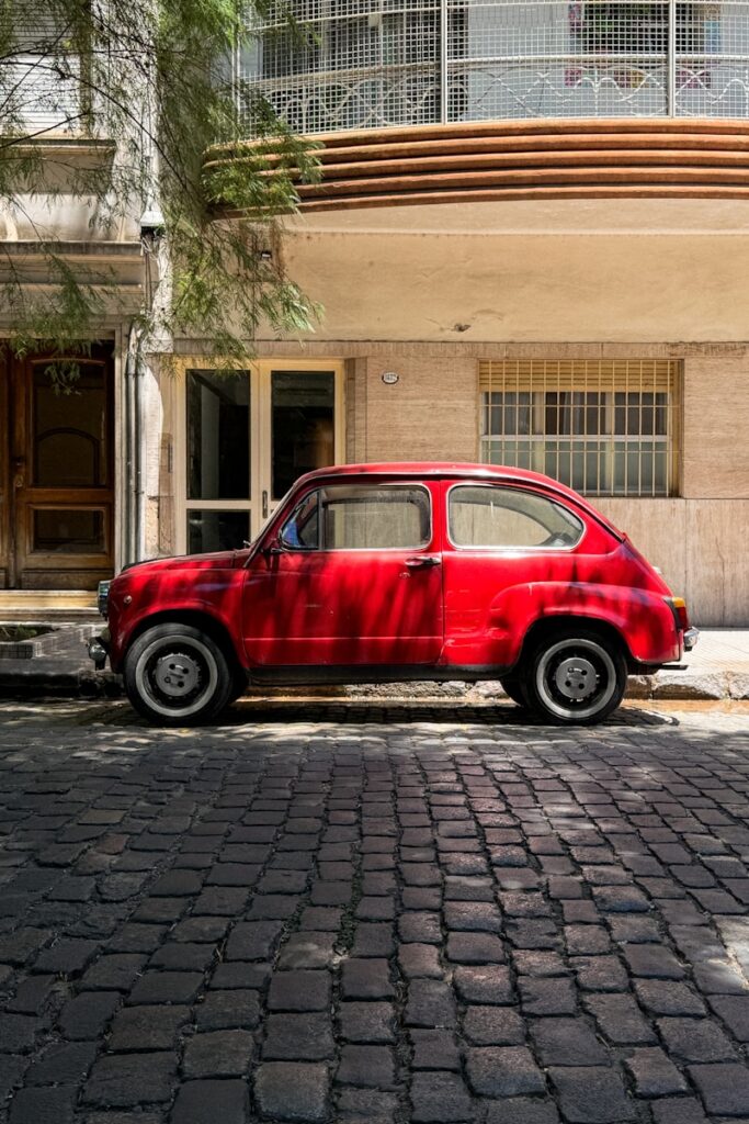 A vintage red car parked on a cobblestone street.