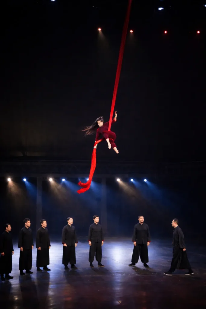Acrobate suspendue à un tissu aérien rouge au-dessus de la troupe, Odyssée