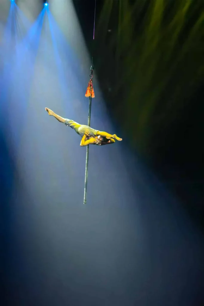 Acrobate à l'horizontale sur une perche suspendue dans un faisceau bleu, mât aérien d'Odyssée
